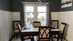 Una sala menjador amb una taula rectangular i sis cadires, una finestra amb cortines, i un quadre de paisatge urbà a la paret.