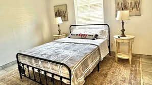 A neatly arranged bedroom with a bed, two bedside tables, a window with blinds, and two wall-mounted lamps. - BALLOON FESTIVAL experience ABQ in style newly renovated 2BD/1BA apartment (Albuquerque)