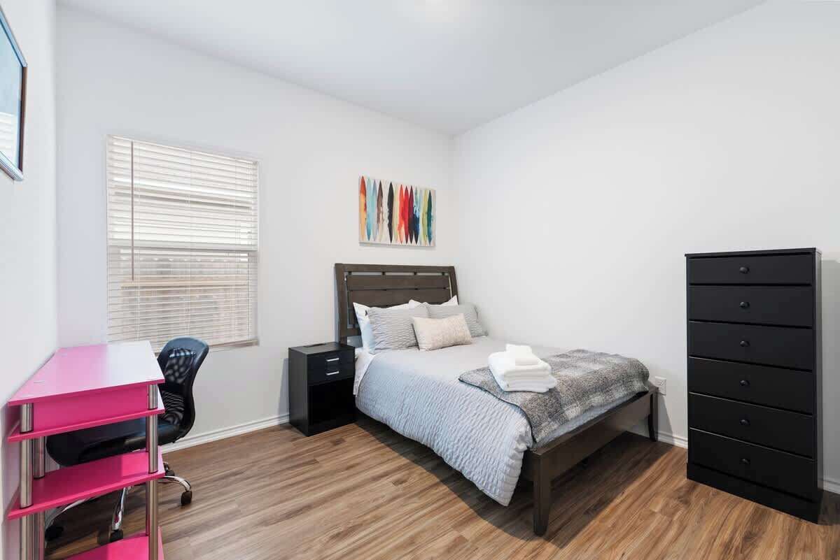 Un dormitorio con cama, escritorio, silla, cómoda y ventana con persianas.