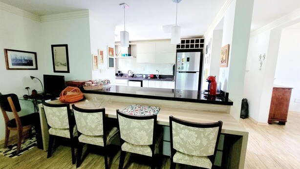 Cozinha moderna com ilha central, banquetas e área de jantar com cadeiras estampadas de flores.