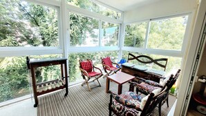Uma sala de sol com grandes janelas, uma mesa de madeira e duas cadeiras de balanço.