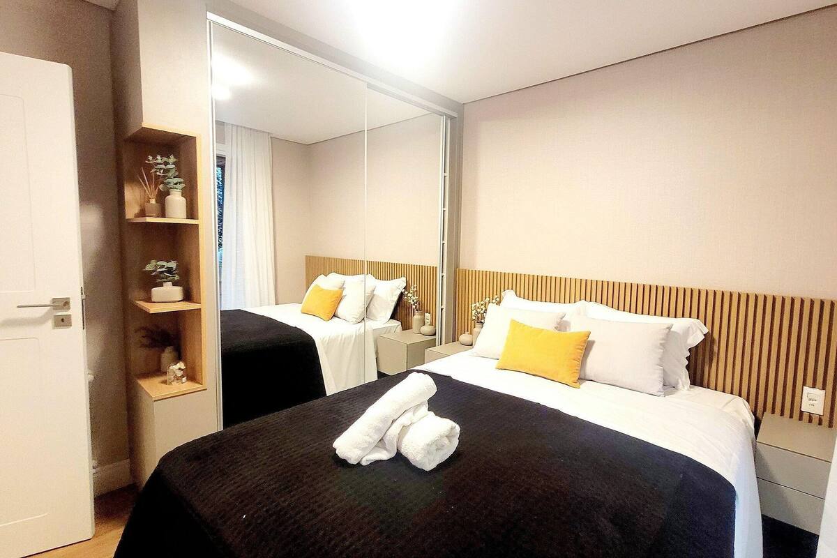 A hotel room with two beds, a large mirror, a shelf with decorative items, and a door.