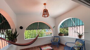Una habitación con una hamaca, dos sillas azules, una mesita y vistas a través de ventanales arqueados.