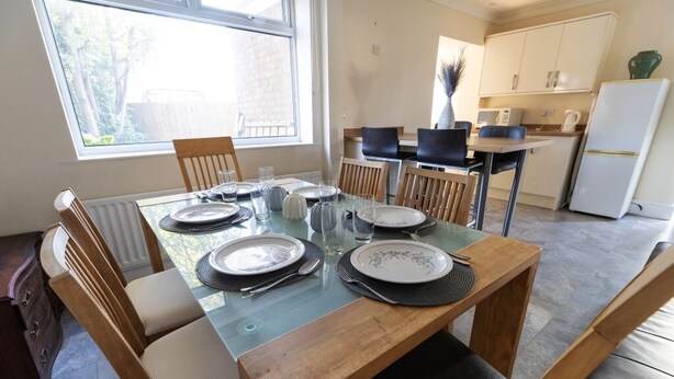 A dining area with a glass table, wooden chairs, and a view of the kitchen in the background. - Charming 3-bedroom house with WiFi and free parking within compound in Thornaby (Thornaby)