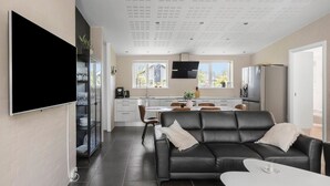 Una sala de estar moderna con un sofá de cuero negro, una mesa de centro blanca y un televisor de pantalla plana montado en la pared.