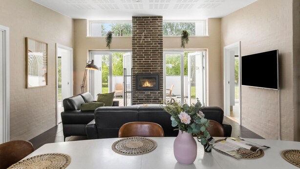 Una sala de estar moderna con chimenea, un comedor con mesa blanca y un televisor montado en la pared.