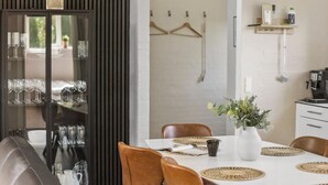 Comedor con una mesa blanca, sillas marrones y un aparador de vidrio con copas de vino.