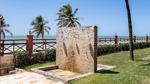 Un sendero pavimentado con un muro de piedra y palmeras, que conduce a una playa bajo un cielo azul despejado.