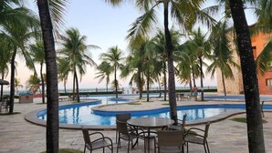 Zona de piscina con palmeras, sillas de descanso y vistas al océano.