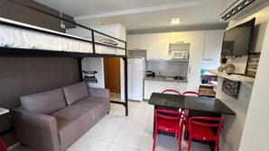 Espaço compacto com cama de solteiro, cozinha compacta, área de refeições e sofá.