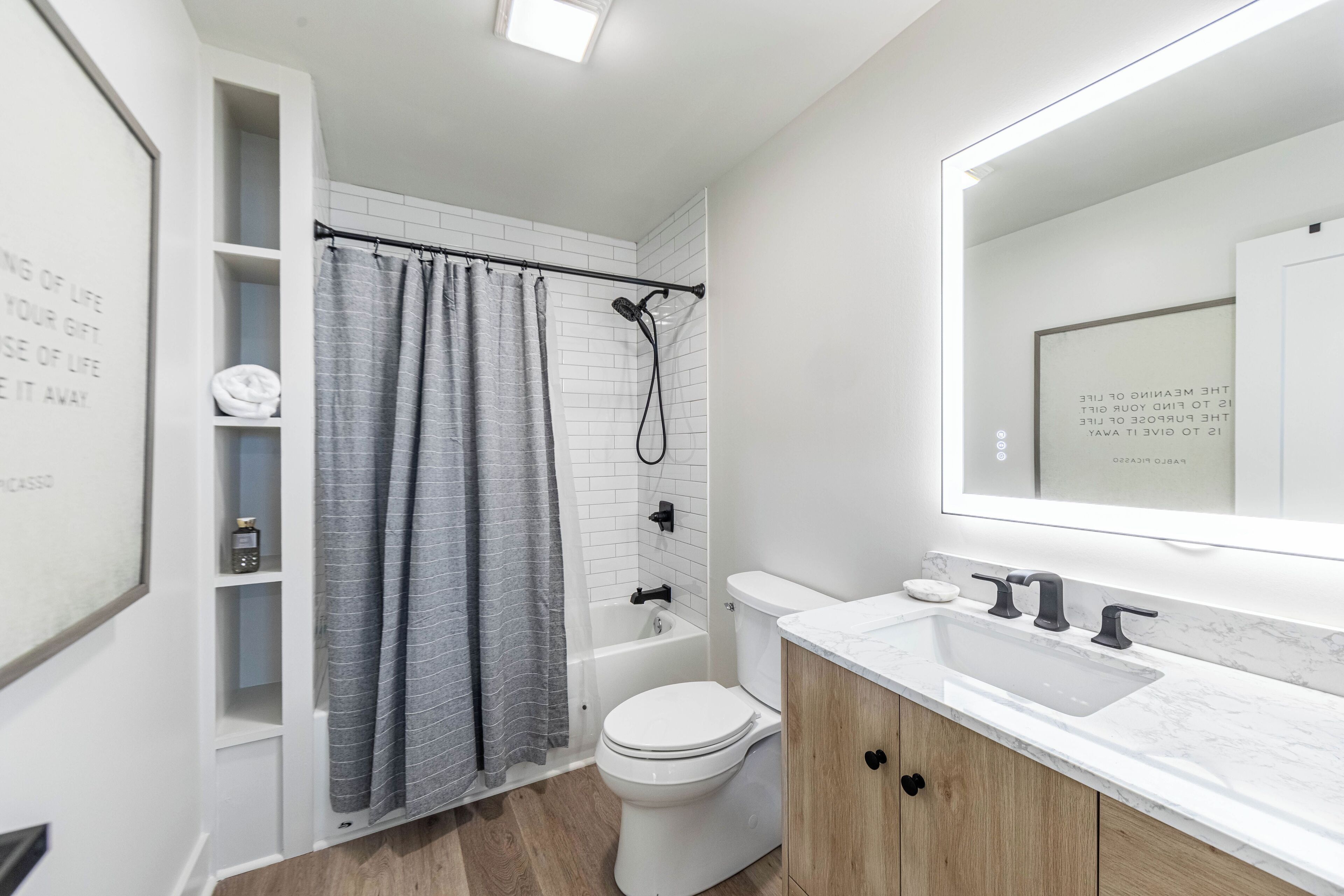 A modern bathroom with a white toilet, a bathtub, a shower, a vanity with a sink, and a mirror.