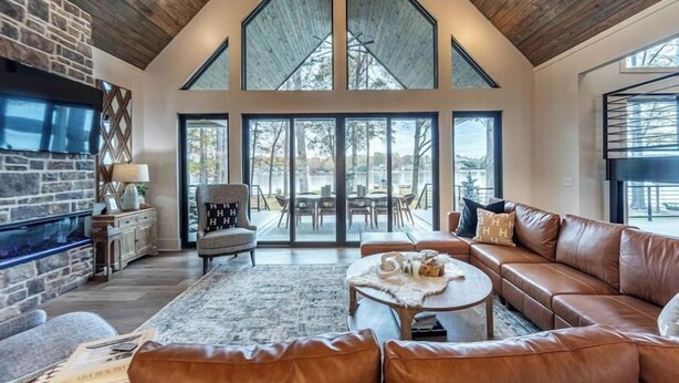 Ein großzügiges Wohnzimmer mit Kamin aus Stein, einer Ledersofa und großen Fenstern mit Blick ins Freie.