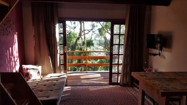 A room with a bed, a table, and a large window with a view of trees.