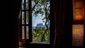 A window with a view of a mountain and trees, curtains partially drawn, and a woven basket on the windowsill.