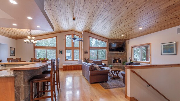 A spacious living area with a stone fireplace, wooden ceiling, and large windows. - *New* Tahoe Donner Cabin*Swiss Chalet* (Truckee)