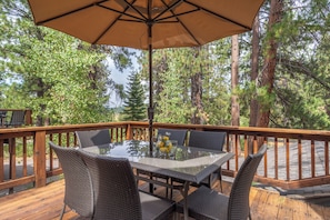 An outdoor deck with a glass-top table and wicker chairs, surrounded by a wooden railing and a large umbrella.