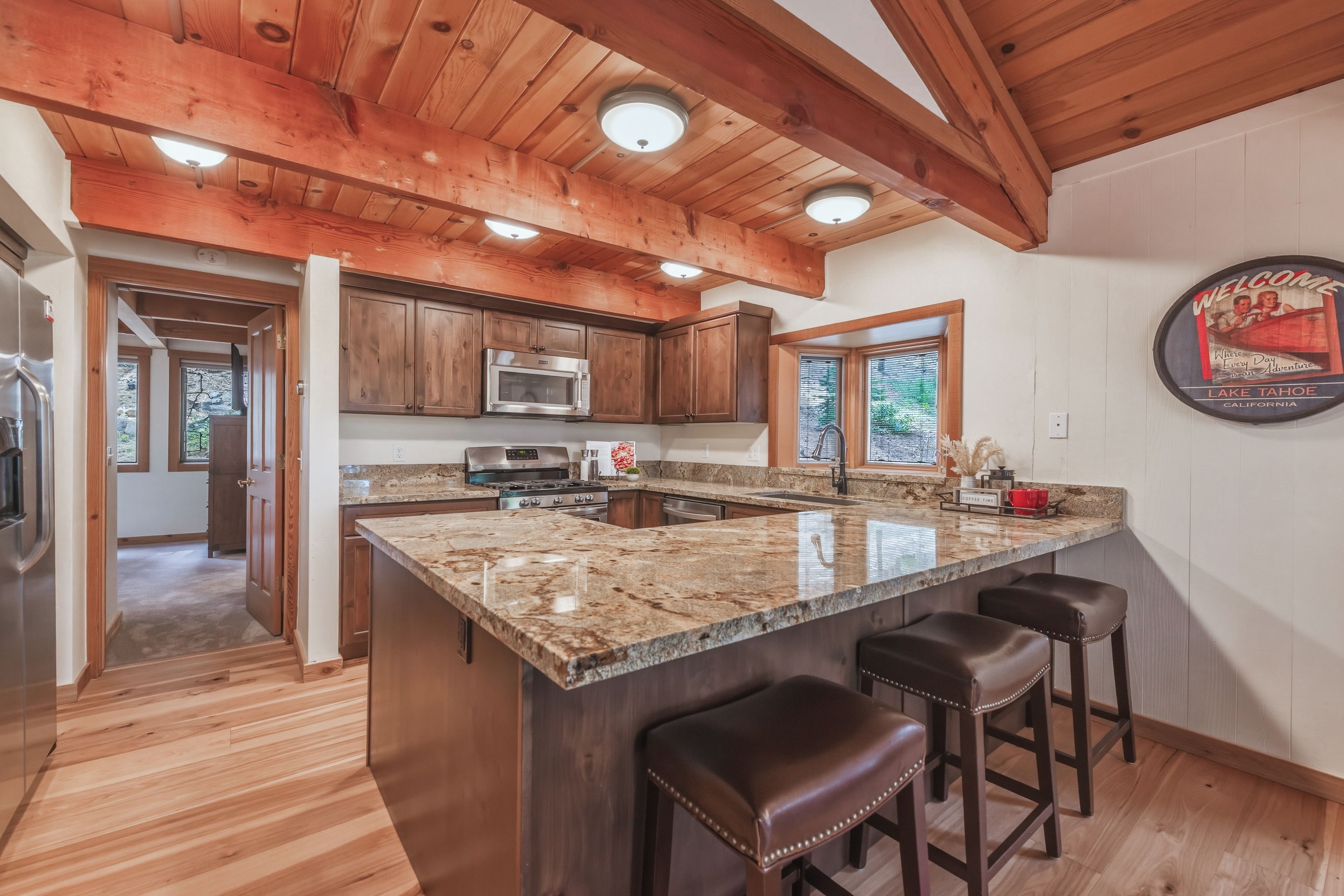 A kitchen with wooden ceiling beams, granite countertops, stainless steel appliances, and a bar area with stools.