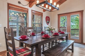 Un comedor con una mesa de madera dispuesta para seis personas, flanqueada por sillas con cojines a cuadros.