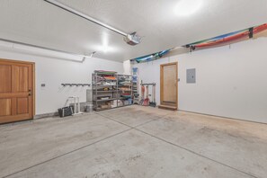 Un garaje con piso de concreto, puerta de madera y un estante metálico guardando diversos objetos.