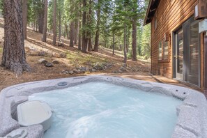 A hot tub surrounded by a forested area with a wooden cabin in the background. - Cozy Northstar Home ~Northstar Mountain~ (Truckee)