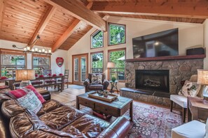 A spacious living room with a stone fireplace, leather sofa, dining area, and large windows. - Cozy Northstar Home ~Northstar Mountain~ (Truckee)