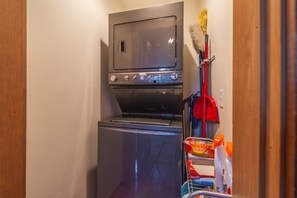 A compact laundry room with a washer and dryer, a broom, and cleaning supplies. - Cozy Northstar Home ~Northstar Mountain~ (Truckee)