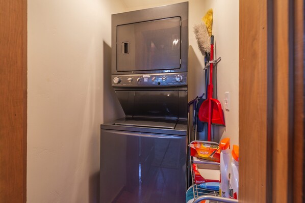 A compact laundry room with a washer and dryer, a broom, and cleaning supplies. - Cozy Northstar Home ~Northstar Mountain~ (Truckee)