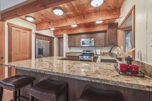 Una cocina con una isla grande, techo de madera, electrodomésticos de acero inoxidable y una zona de bar con taburetes.