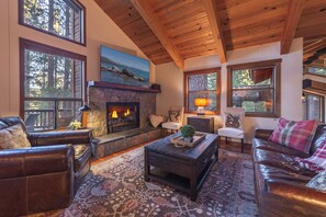 Una sala de estar acogedora con sofás de cuero, chimenea y ventanas amplias con vista a árboles.