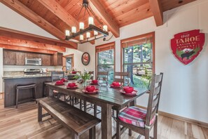 A wooden interior with a dining table set for four, a kitchen area, and a view of the outdoors. - Cozy Northstar Home ~Northstar Mountain~ (Truckee)