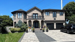 A two-story house with a brick exterior, a front porch with a railing, and a driveway leading to a garage. - Luxurious home with indoor pool and spa (Brossard)