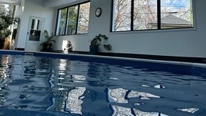 A modern indoor swimming pool with skylights, large windows, and potted plants. - Luxurious home with indoor pool and spa (Brossard)