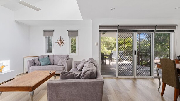 A modern living room with a grey sofa, a wooden coffee table, and a dining area with a chair. - Beachside Family Haven (Inverloch)