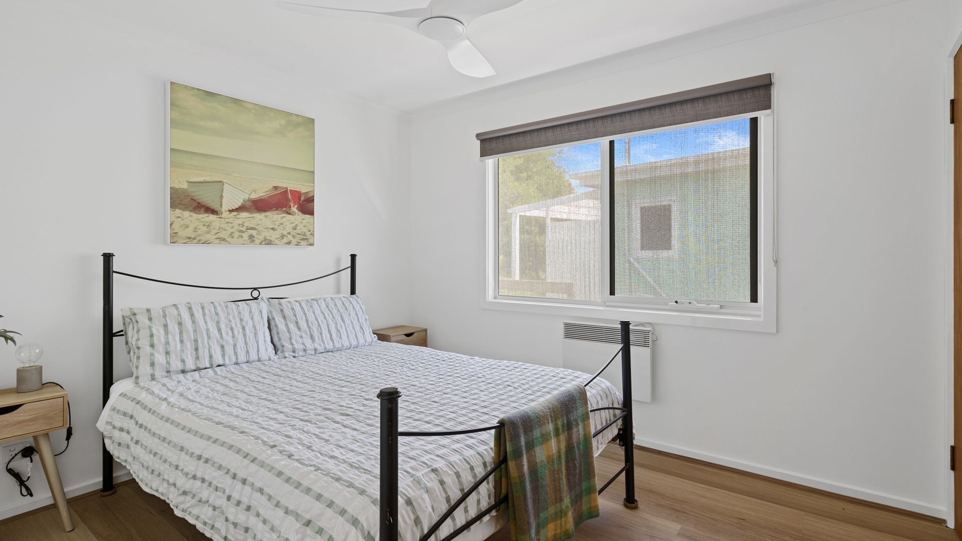 A bedroom with a bed, a nightstand, a window with a view, and a ceiling fan.