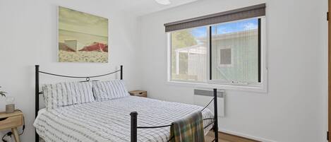 A bedroom with a bed, a nightstand, a window with a view, and a ceiling fan.