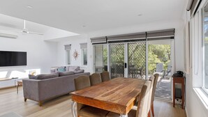 A modern living room with a wooden dining table, grey sofa, and a TV. - Beachside Family Haven (Inverloch)