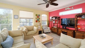 A living room with a beige sofa set, a wooden coffee table, a television, and a decorative shelf with seashells. - Island Living Awaits at Sand Dollar Villa Three Bedroom/Two Bath STEPS from GULF BEACHES!! (Bradenton Beach)