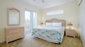 A bedroom with a large bed, a dresser, a mirror, and a balcony. - Island Living Awaits at Sand Dollar Villa Three Bedroom/Two Bath STEPS from GULF BEACHES!! (Bradenton Beach)