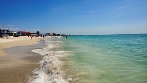 A beach with clear turquoise water, sandy shore, and umbrellas. - Island Living Awaits at Sand Dollar Villa Three Bedroom/Two Bath STEPS from GULF BEACHES!! (Bradenton Beach)
