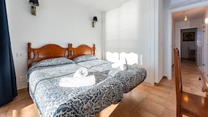 Un dormitorio con cama de madera, ropa de cama estampada, lámparas fijadas a la pared y vistas a un pasillo.