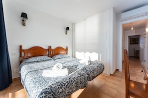Un dormitorio con cama de madera, ropa de cama estampada, lámparas fijadas a la pared y vistas a un pasillo.