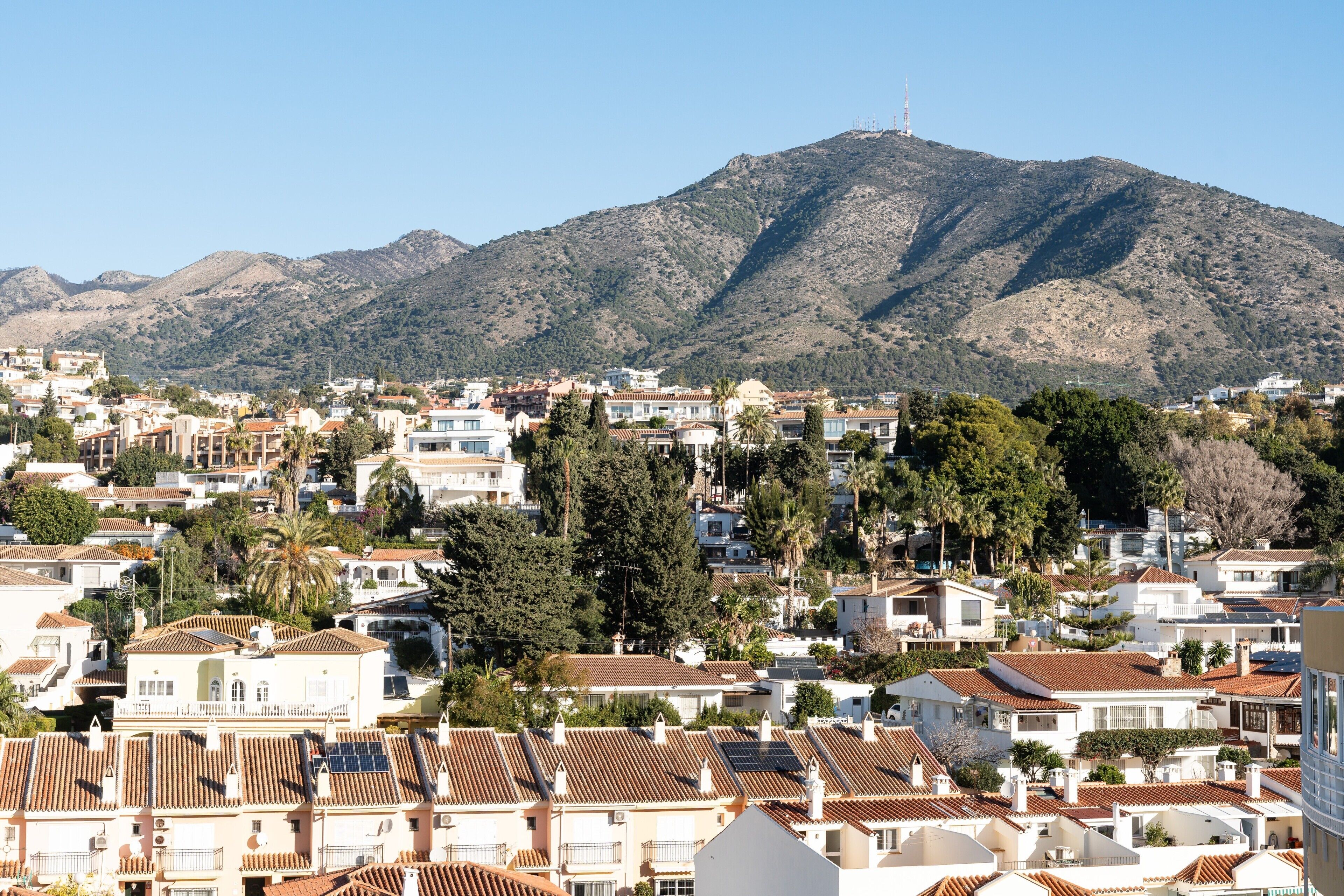 A residential area with houses, some with solar panels, and a mountain in the background.