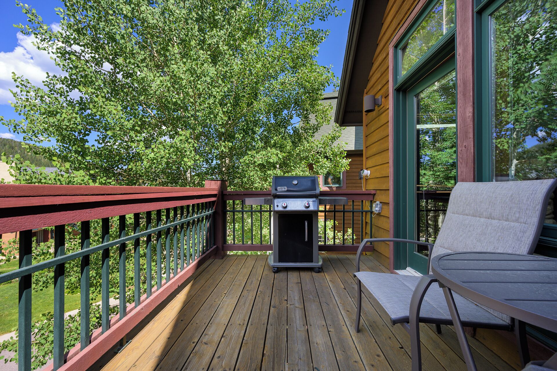 A wooden deck with a grill, a chair, and a view of trees.