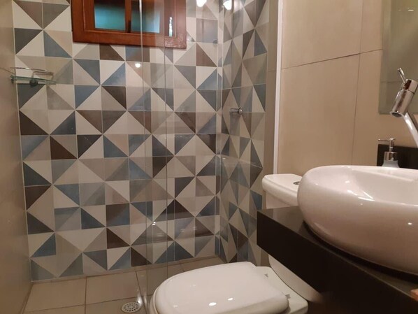 Un baño con un revestimiento de azulejos geométricos, un inodoro blanco y un lavabo redondo con un espejo encima.