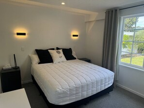 Ein Schlafzimmer mit einem Bett, zwei Nachttischen, einem Fenster mit Vorhängen und Wandleuchten.