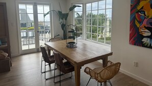 A dining area with a wooden table and chairs, large windows, and a view of the outdoors.