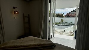 A bedroom with a bed, a window, and a view of an outdoor swimming pool.