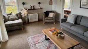 A cozy living room with a fireplace, a sofa, a chair, and a coffee table. - Three Fifty Cottage (Havelock North)
