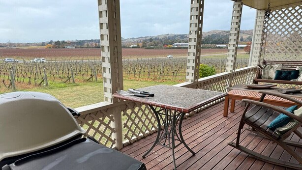 A wooden deck with a table and chairs, overlooking a vineyard. - Three Fifty Cottage (Havelock North)