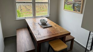 A room with a wooden table, a bench, and a window with a vineyard view. - Three Fifty Cottage (Havelock North)